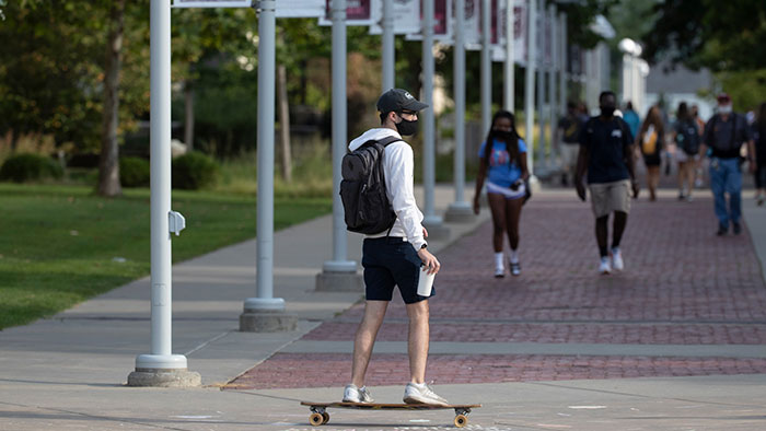 Student skateboarding through campus with mask