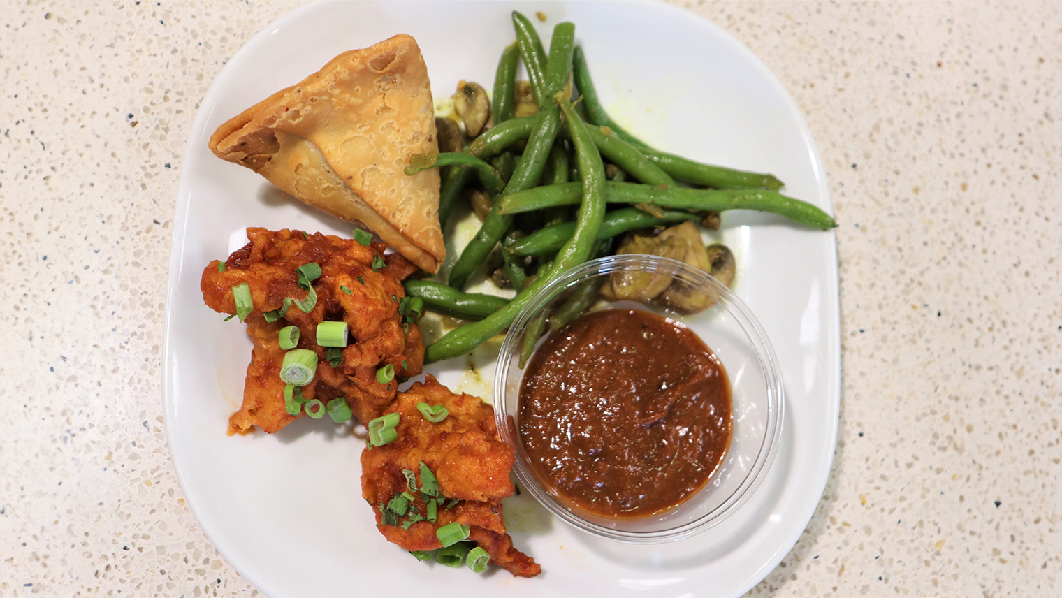 chicken wings samosa and green beans with sauce on white plate